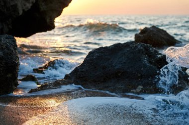 Splash dalgalar güzel gün batımı ve gökyüzü ile kayalara çarptı                               