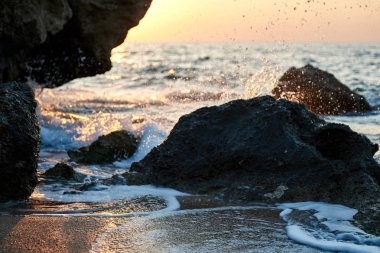 Günbatımı deniz kenarında. Altın kumlar. Dalgalar deniz kumları ve kayalar üzerinde rulo.                               
