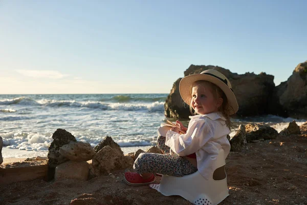 Kumlu sahilde bir kitap okuma güzel küçük bir kız. O yanında pot oturuyor ve uzak gülümseme kitap arıyorum.                              