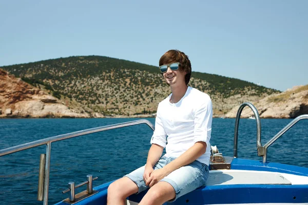Portrait of a young successful man on the background of sky and sea landscape.  with glasses in white shirt leaning on the railing of the ship. Cruise.