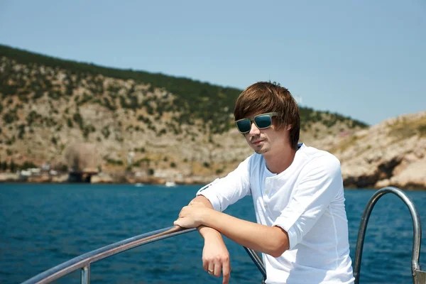 Portrait of a young successful man on the background of sky and sea landscape.  with glasses in white shirt leaning on the railing of the ship. Cruise.