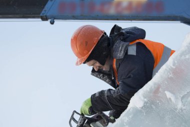 Ellerinde elektrikli testereyle koruyucu bir miğfer takmış işçi derleyicisi buz kalıbını keser.