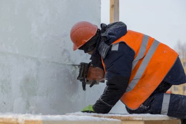 Ellerinde elektrikli testereyle koruyucu bir miğfer takmış işçi derleyicisi buz kalıbını keser.