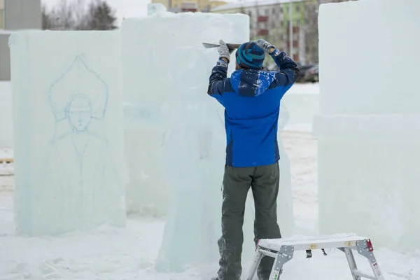 The sculptor cuts an ice figure for Christmas from a block of ice with a chisel