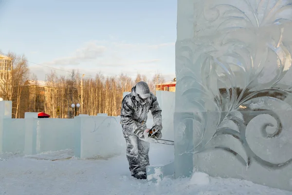 The sculptor cuts ice contours from ice with a chainsaw for Christmas