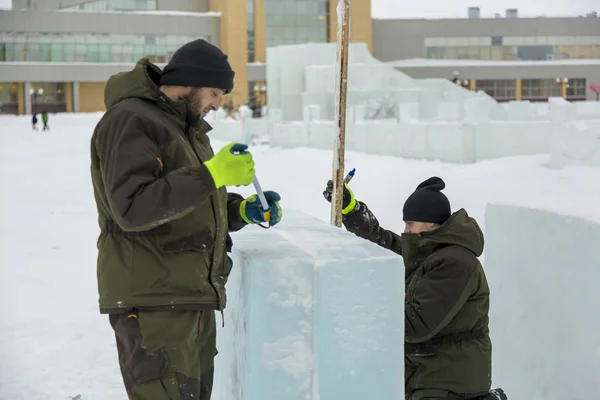 Workers assemblers mark the ice block on the construction site of the ice town