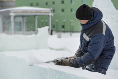 İşçi buz şehrin montaj yerinde elinde testere ile