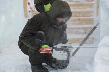 Elinde elektrikli testereyle çalışan bir işçi, buz bloğunun altını oyuyor.