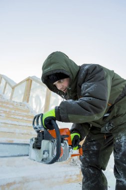 Elinde elektrikli testereyle çalışan bir işçi, buz bloğunun altını oyuyor.