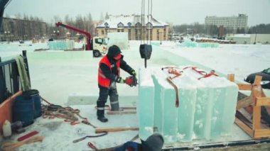 Koruyucu miğfer ve yansıtıcı yelek giyen bir işçi buz bloğunda benzopil ile bir delik açıyor.