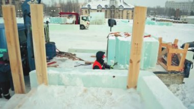 Turuncu yelekli bir işçi arabasından buz parçaları indirmekle meşgul..