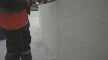 İşçi, buz panelini benzin testeresiyle kesiyor. Turuncu yansıtıcı yelek ve miğfer takıyor. Elektrikli testere buz kalıbını özelleştiriyor.