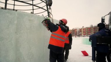 İşçi, buz panelini benzin testeresiyle kesiyor. Turuncu yansıtıcı yelek ve miğfer takıyor. Elektrikli testere buz kalıbını özelleştiriyor.