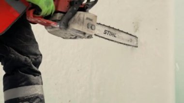 Elinde elektrikli testere ile turuncu yelekli bir tesisatçının portresi Koruyucu kask ve yansıtıcı yelek ile bir tesisatta çalışan bir işçi, buz bloğunda bir benzopil ile delik açar.