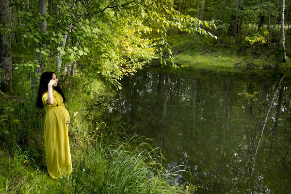 Portrait of a pregnant woman in a yellow dress in the autumn forest