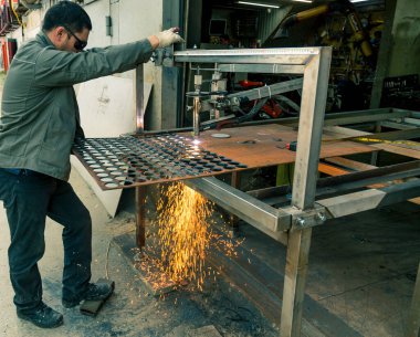 Bir işçi plazma makinesiyle kalın bir levha keser. Erimiş çelik damlalarını farklı yönlere saçarlar.