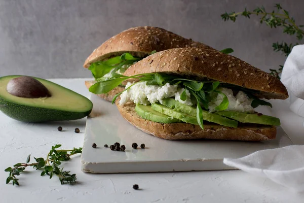 Beyaz Rustik seramik kesme tahtasında avokado ve ricotta peynir ile tüm tahıl gluten ücretsiz ev yapımı ekmek yapılmış iki sandviç. Sağlıklı ev yapımı gıda konsepti 