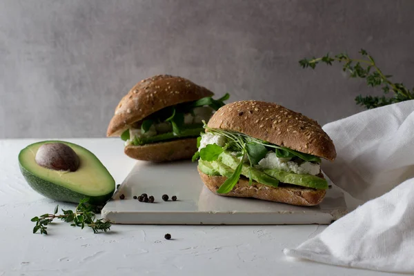 Beyaz Rustik seramik kesme tahtasında avokado ve ricotta peynir ile tüm tahıl gluten ücretsiz ev yapımı ekmek yapılmış iki sandviç. Sağlıklı ev yapımı gıda konsepti 