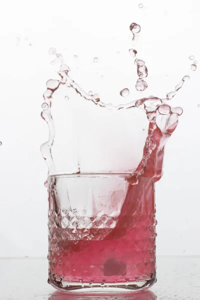 Beyaz arka planda sıçramaları olan bir bardak taze içki. Dondurulmuş hareket. Trendy renk 2019, mercan