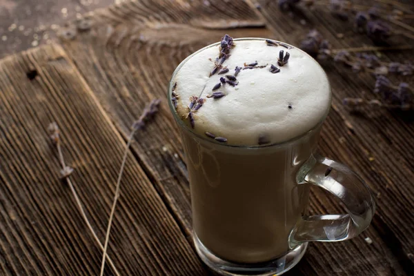 Low key photo of lavender latte or raf coffee in transparent cup with lavender twigs on background, close up, back light. Trendy dark and moody style