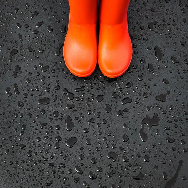 The edges of the orange rain boots are on a wet wet surface covered with raindrops. Top view, copy space.