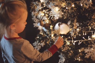 Beyaz bir çekici kız bir şekilde dekore edilmiş Noel ağacı ve ışıklar üzerinde inceliyor. Aile dostu Noel kavramı.