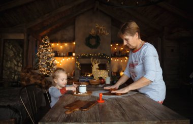 Genç bir büyükanne ve güzel sarışın torunuyla birlikte Noel için dekore edilmiş bir evde kurabiye pişirin. Aile Noel kavramı.