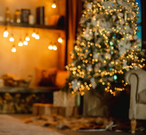 Home background. Christmas tree with gifts and reading corner decorated with garlands. Blurred.