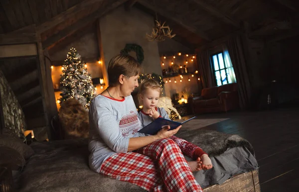 Grandma and granddaughter have fun together reading a book on the bed . Family Christmas concept.