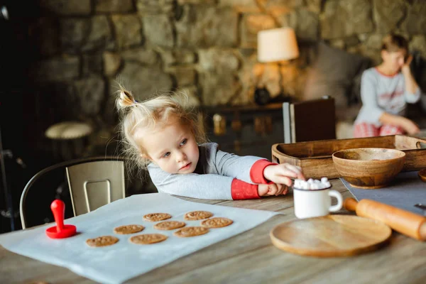 A charming little girl reaches for marshmallows in a Cup of cocoa, which stands on a table with Christmas cookie