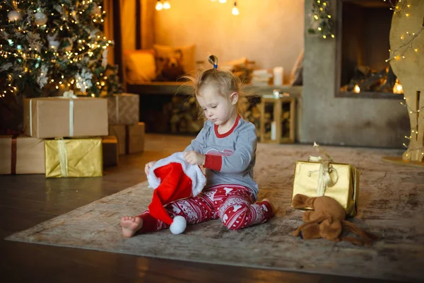Kis Szőke Kisgyermek Lány Karácsonyi Pizsamában Mikulás Kalapját Otthon Szőnyegen — Stock Fotó