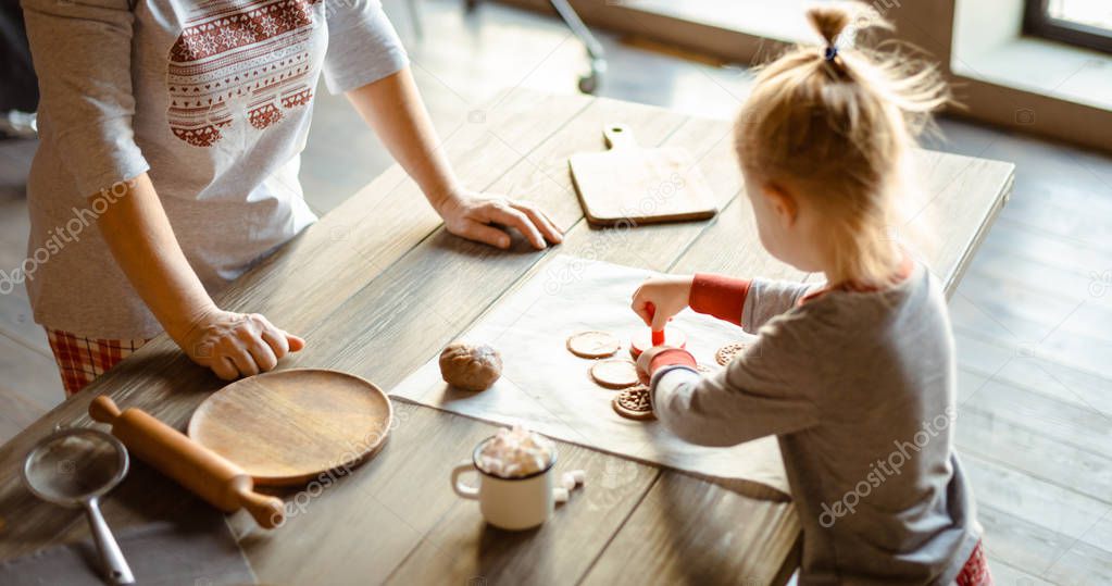 Grandmother and granddaughter in the morning in the same pajamas together bake Christmas cookies-stamps on the test. The family cozy Christmas concept. Selective focus.