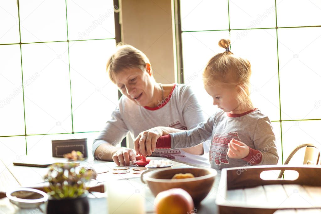 A young grandmother and her lovely blonde granddaughter cook cookies together in a house decorated for Christmas. Family concept of Christmas.