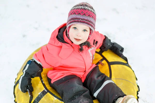美丽的小女孩在冬天的衣服坐在雪管上 看着相机 — 图库照片