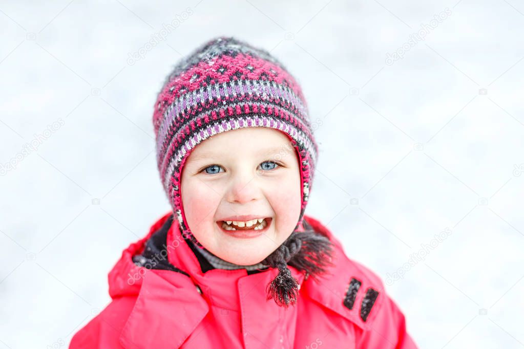 A pretty white girl in a knitted winter hat and pink jumpsuit, smiling and laughing in the snow . Portrait close-up.