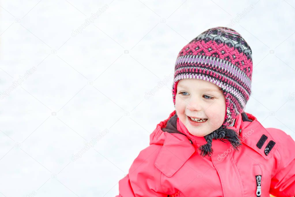 A pretty white girl in a knitted winter hat and pink jumpsuit, smiling and laughing in the snow . Portrait close-up.