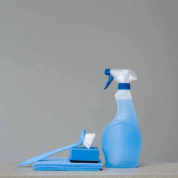 Cleaning blue spray bottle with plastic dispenser, sponge, 	scrubbing brush for dish and cloth for dust  on grey background. Cleaning tools. Copy space.