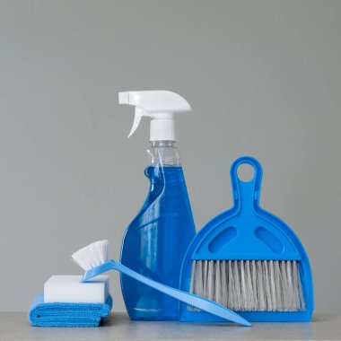 Blue cleaning kit on neutral background: Spray detergent, dishwashing brush, dust cloths, sponge, scoop and broom. Copy space. clipart
