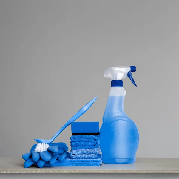 Cleaning blue spray bottle with plastic dispenser, sponge, 	scrubbing brush for dish, cloth for dust and rubber gloves  on grey background. Cleaning equipment. Copy space.