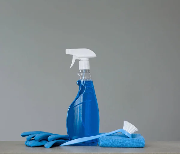 Cleaning blue spray bottle with plastic dispenser, scrubbing brush for dish, cloth for dust and rubber gloves  on grey background. Cleaning equipment. Copy space.