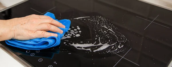 Bir cam seramik Ocak mutfakta bir kadın eli bir mavi mikrofiber bezle losyonları.