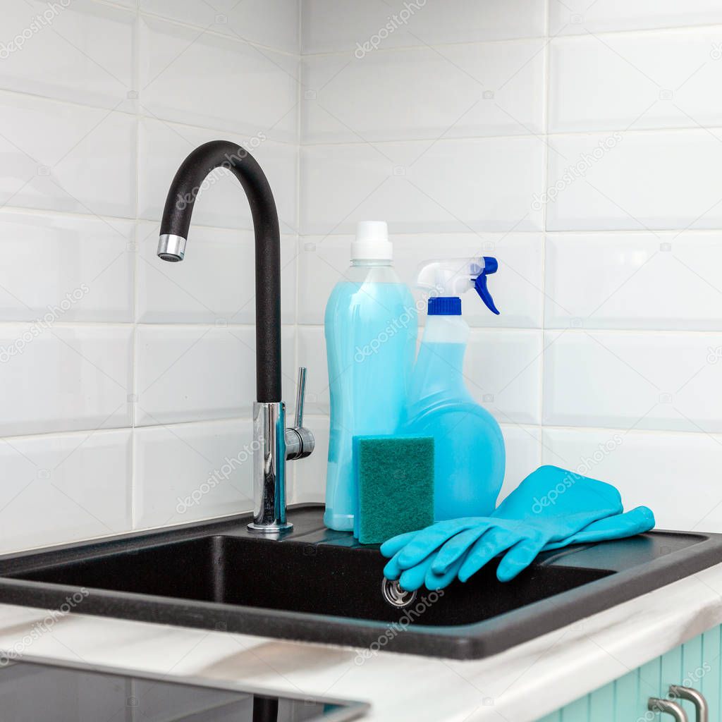 A set of blue cleaning products and tools for cleaning the kitchen is near the kitchen sink.