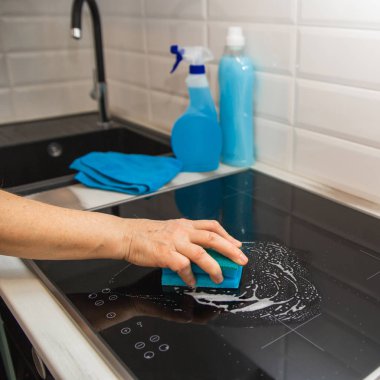 Bir kadın eli mavi bir sünger ile mutfakta bir cam seramik tabak losyonları. Arka plan vardır temizlik ürünleri.