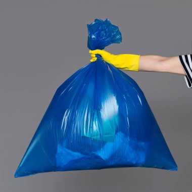 Bir mavi plastik torba çöp dolu bir lastik eldiven bir kadının elinde tutan.