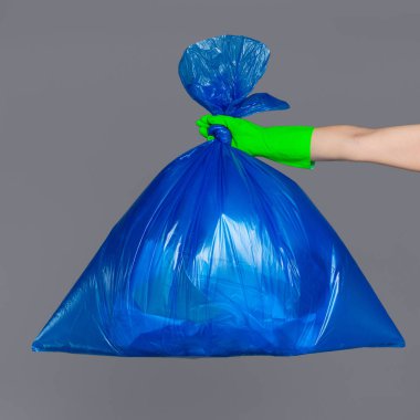 Bir mavi plastik torba çöp dolu bir lastik eldiven bir kadının elinde tutan.