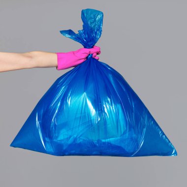 Bir mavi plastik torba çöp dolu bir lastik eldiven bir kadının elinde tutan.