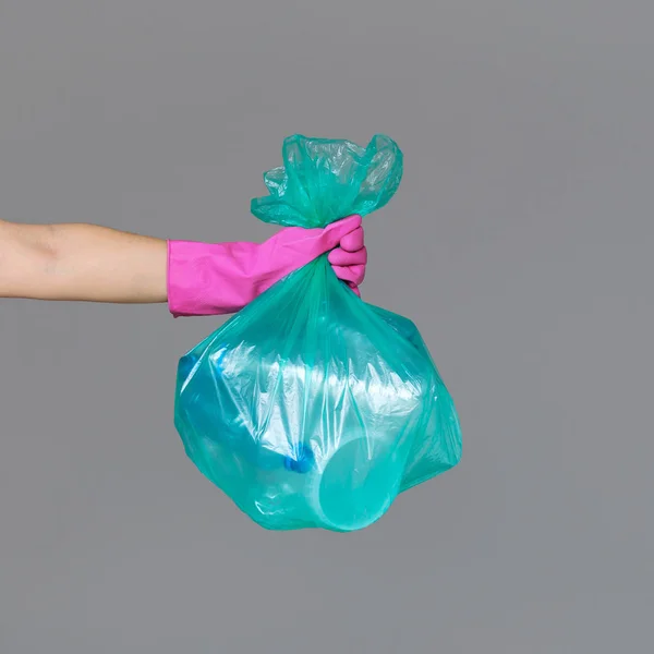 Bir lastik eldiven bir kadın eli boş plastik şişe ile bir şeffaf yeşil çöp torbası tutar. Ekoloji, ayrı atık toplama ve geri dönüşüm kavramı.