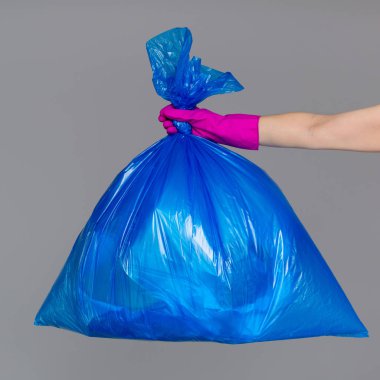 Bir mavi plastik torba çöp dolu bir lastik eldiven bir kadının elinde tutan.