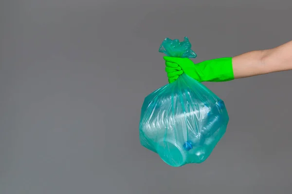 Bir lastik eldiven bir kadın eli boş plastik şişe ile bir şeffaf yeşil çöp torbası tutar. Ekoloji, ayrı atık toplama ve geri dönüşüm kavramı.