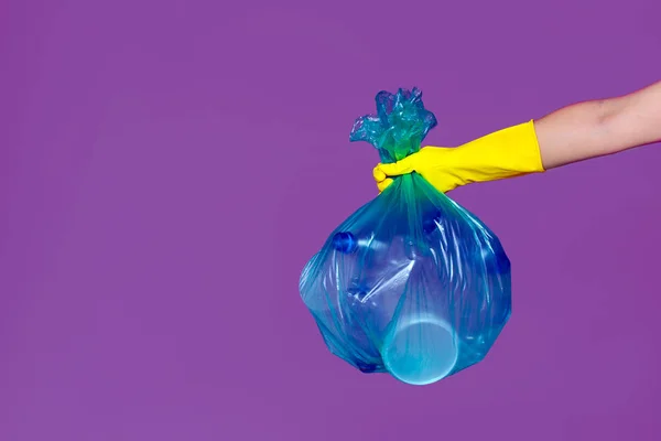 Bir lastik eldiven bir kadın eli boş plastik şişe ile bir şeffaf mavi çöp torbası tutar. Ekoloji, ayrı atık toplama ve geri dönüşüm kavramı.